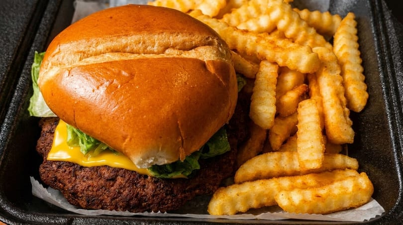 A cheeseburger with lettuce and a side of crinkle-cut fries in a black takeout container.