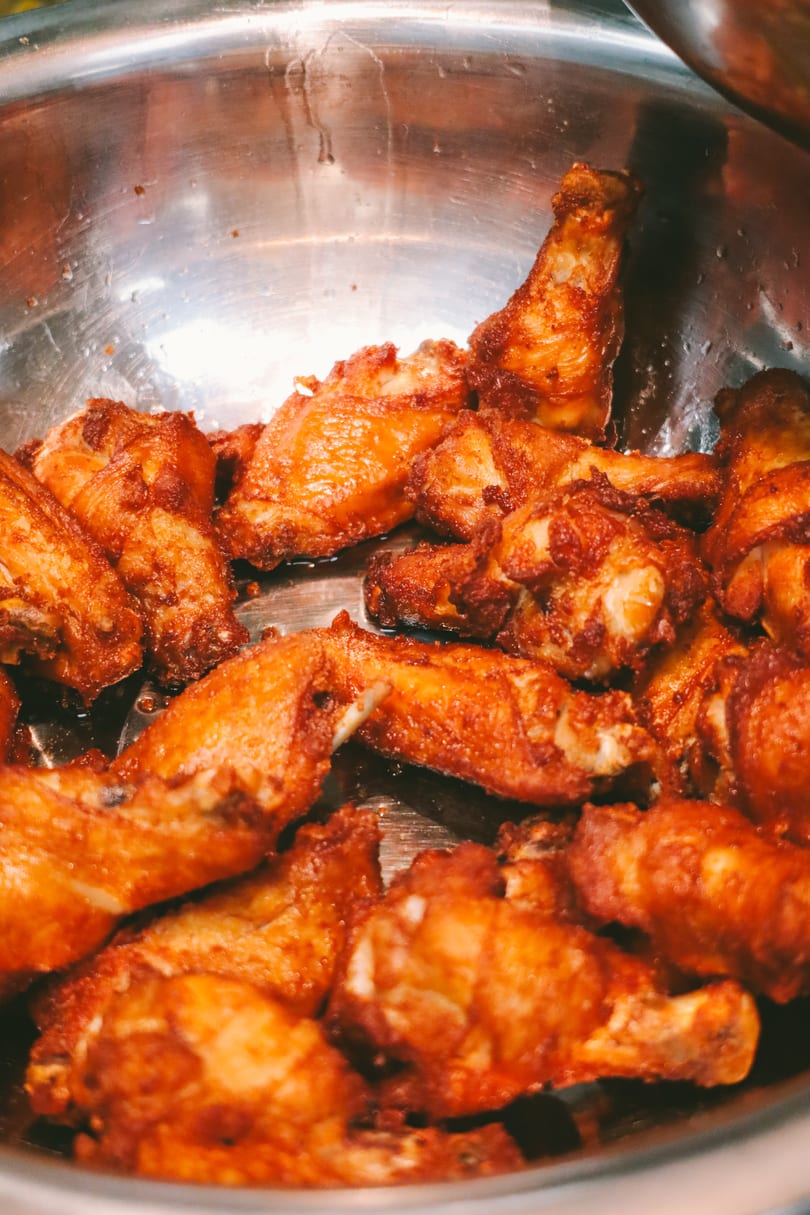 Close-up of crispy, golden-brown fried chicken wings in a large metal bowl.