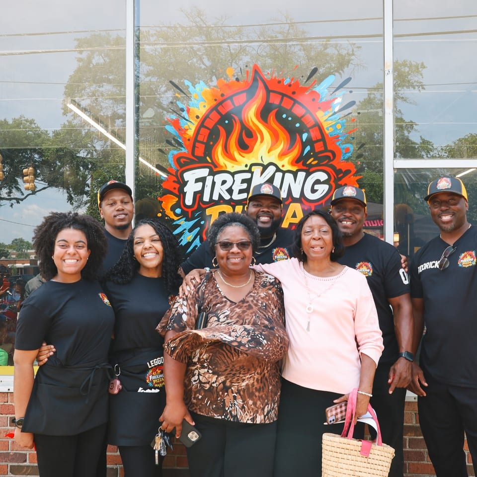The Fire King family holding the red ribbon at the grand opening ribbon cutting.