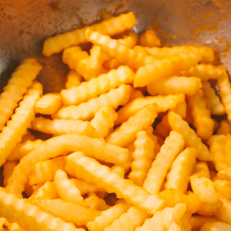 Close-up of golden, crinkle-cut french fries in a metal bowl, seasoned with spices.