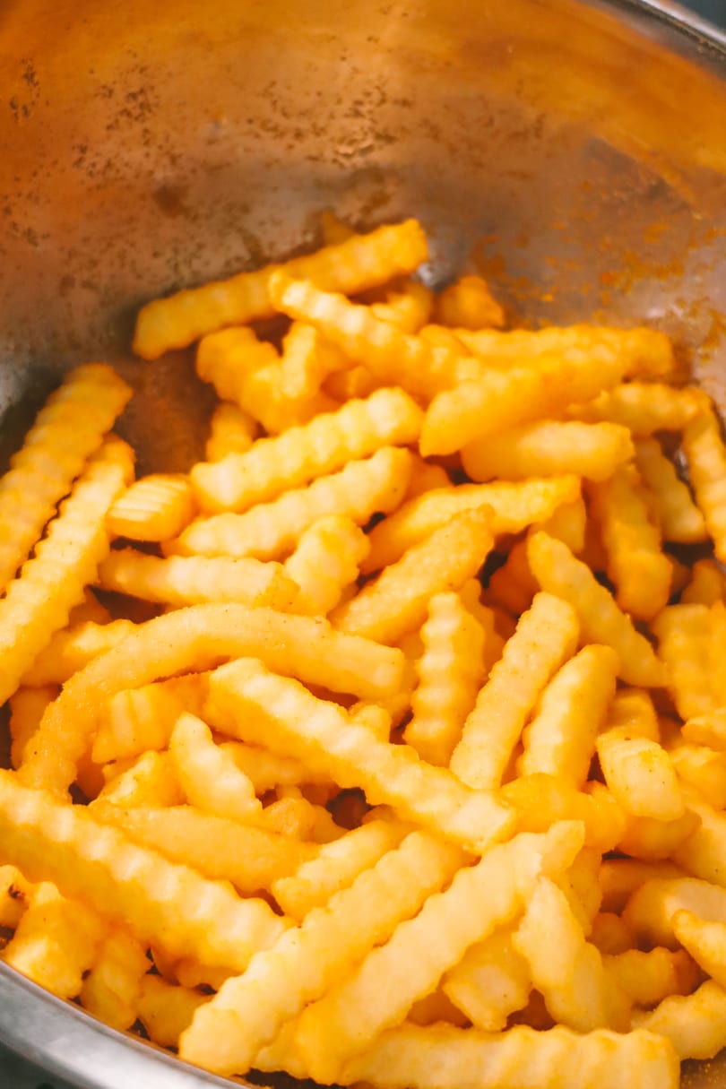 Close-up of golden, crinkle-cut french fries in a metal bowl, seasoned with spices.