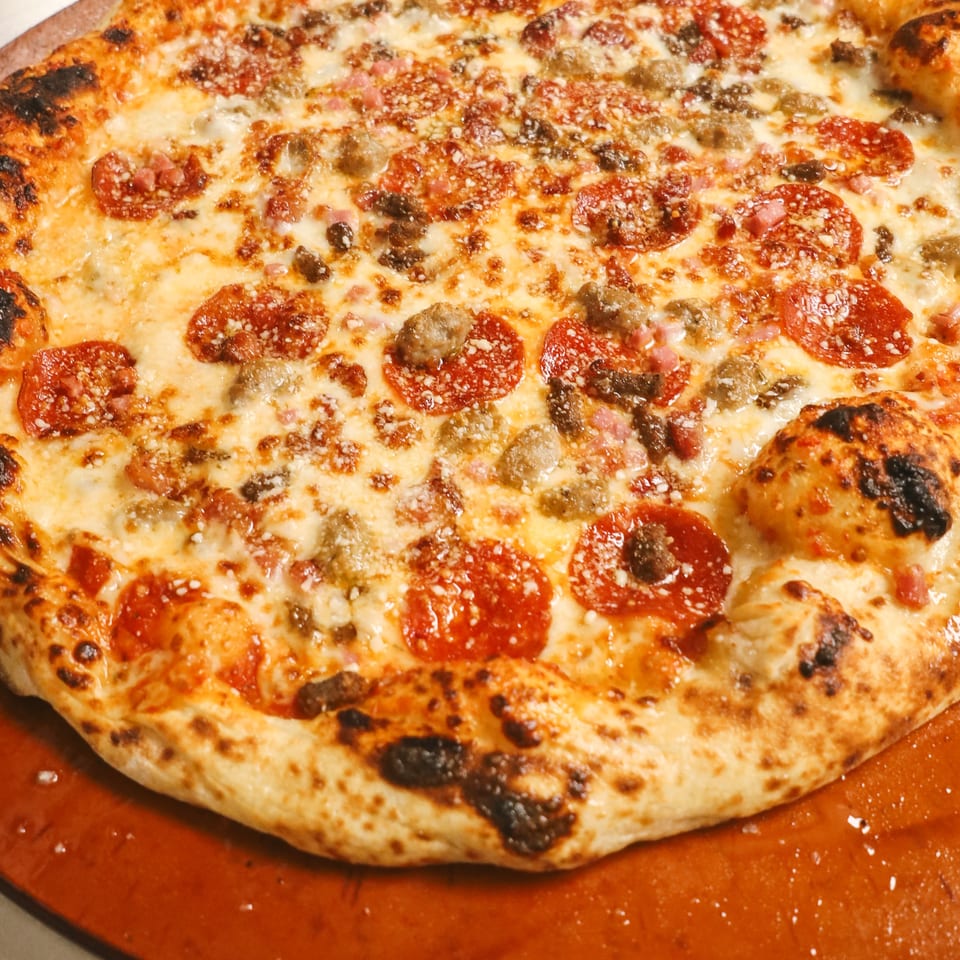 A freshly baked pizza with pepperoni, sausage, and melted cheese on a wooden peel.