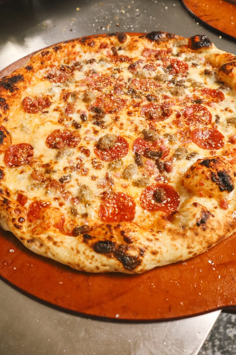 A freshly baked pizza with pepperoni, sausage, and melted cheese on a wooden peel.